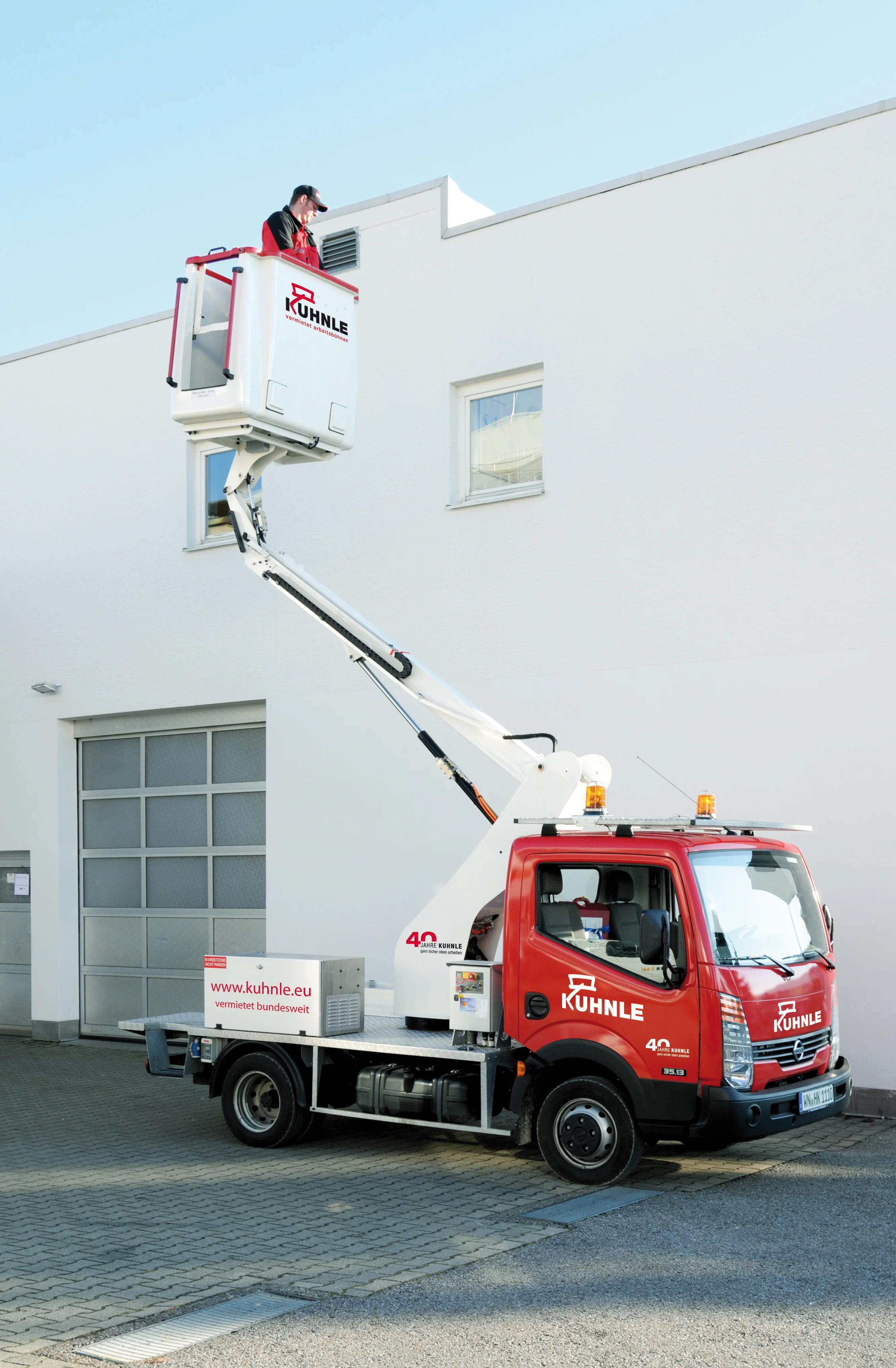 Ausgefahrene Arbeitsbühne vor weißem Gebäude, eine Person darauf.