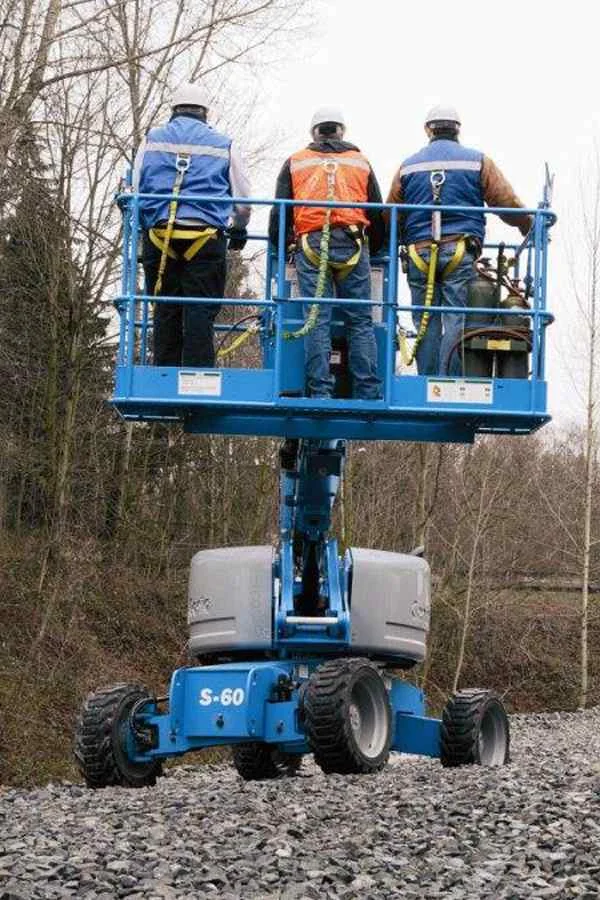 Blaue Arbeitsbühne neben Bäumen, darauf drei Personen mit Schutzkleidung.