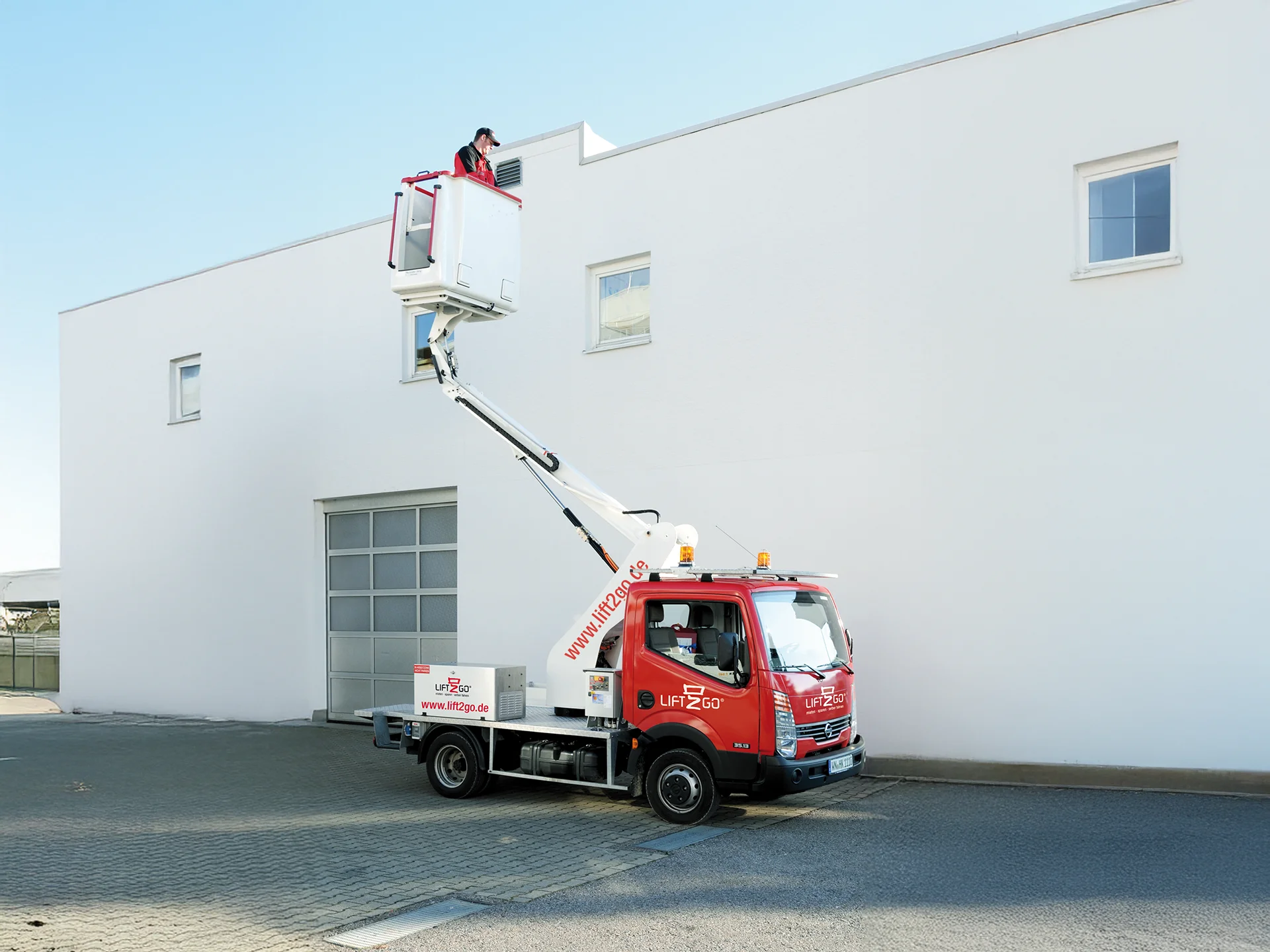 Ausgefahrene Arbeitsbühne vor weißem Gebäude, eine Person darauf.