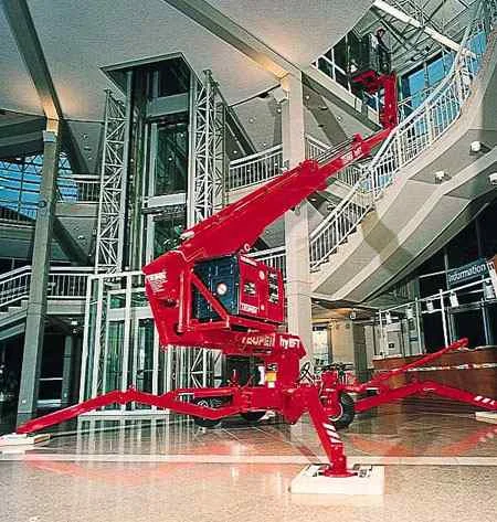 Rote Arbeitsbühne in moderner Halle mit Glasaufzug und Treppen.