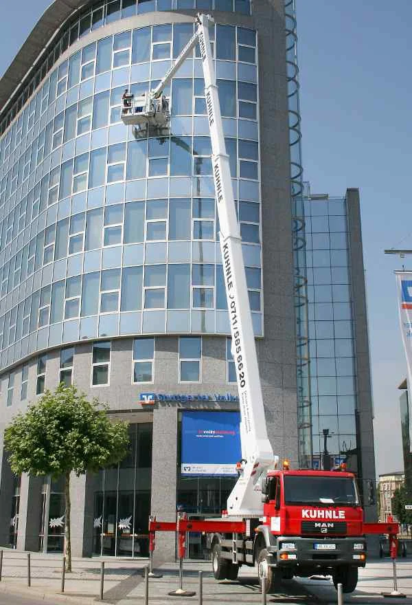 Gehweg vor Gebäude mit Fensterfront, darauf ausgefahrene Arbeitsbühne.