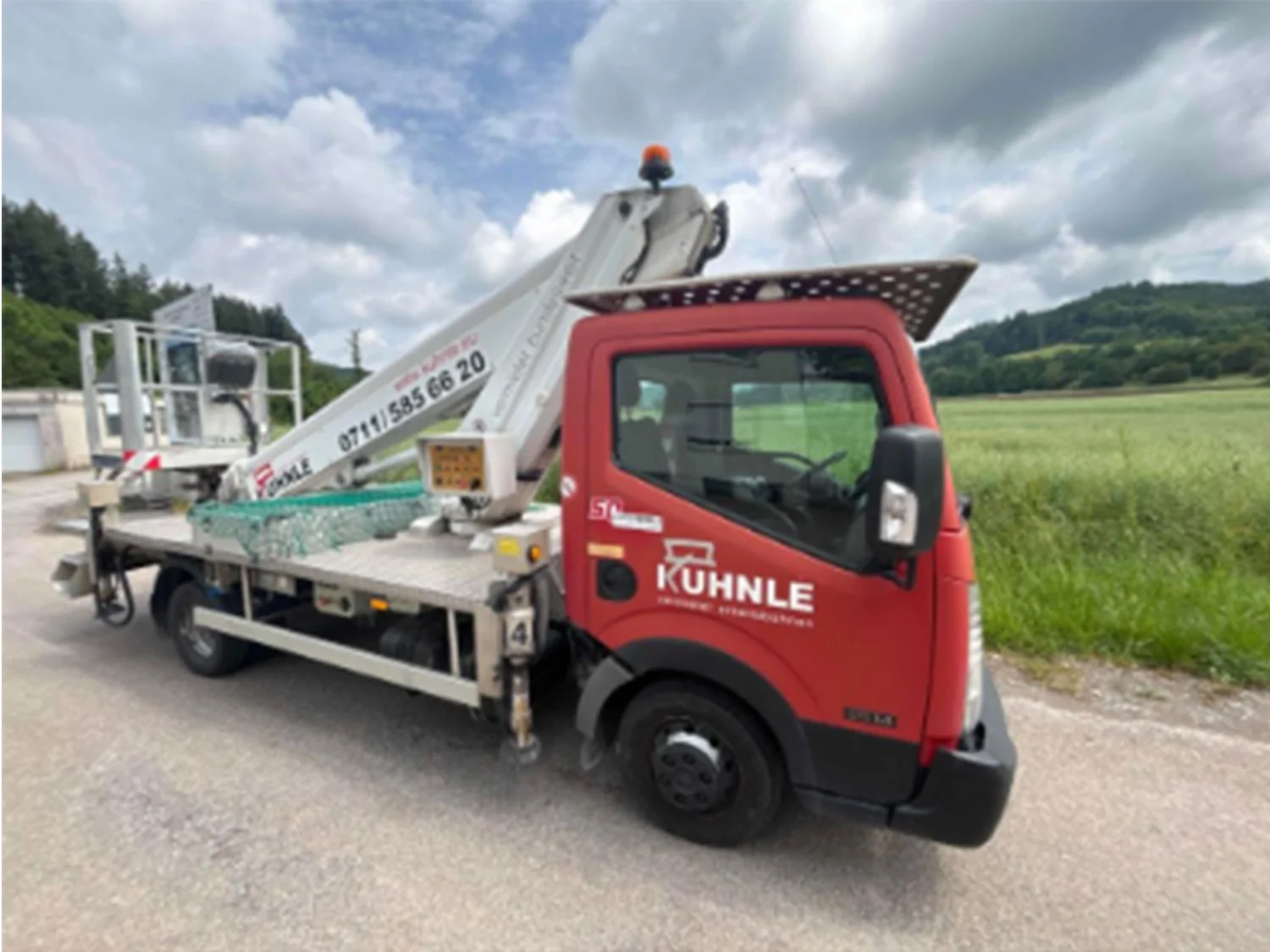 Arbeitsbühne auf Straße, dahinter Feld und Bäume in der Ferne.