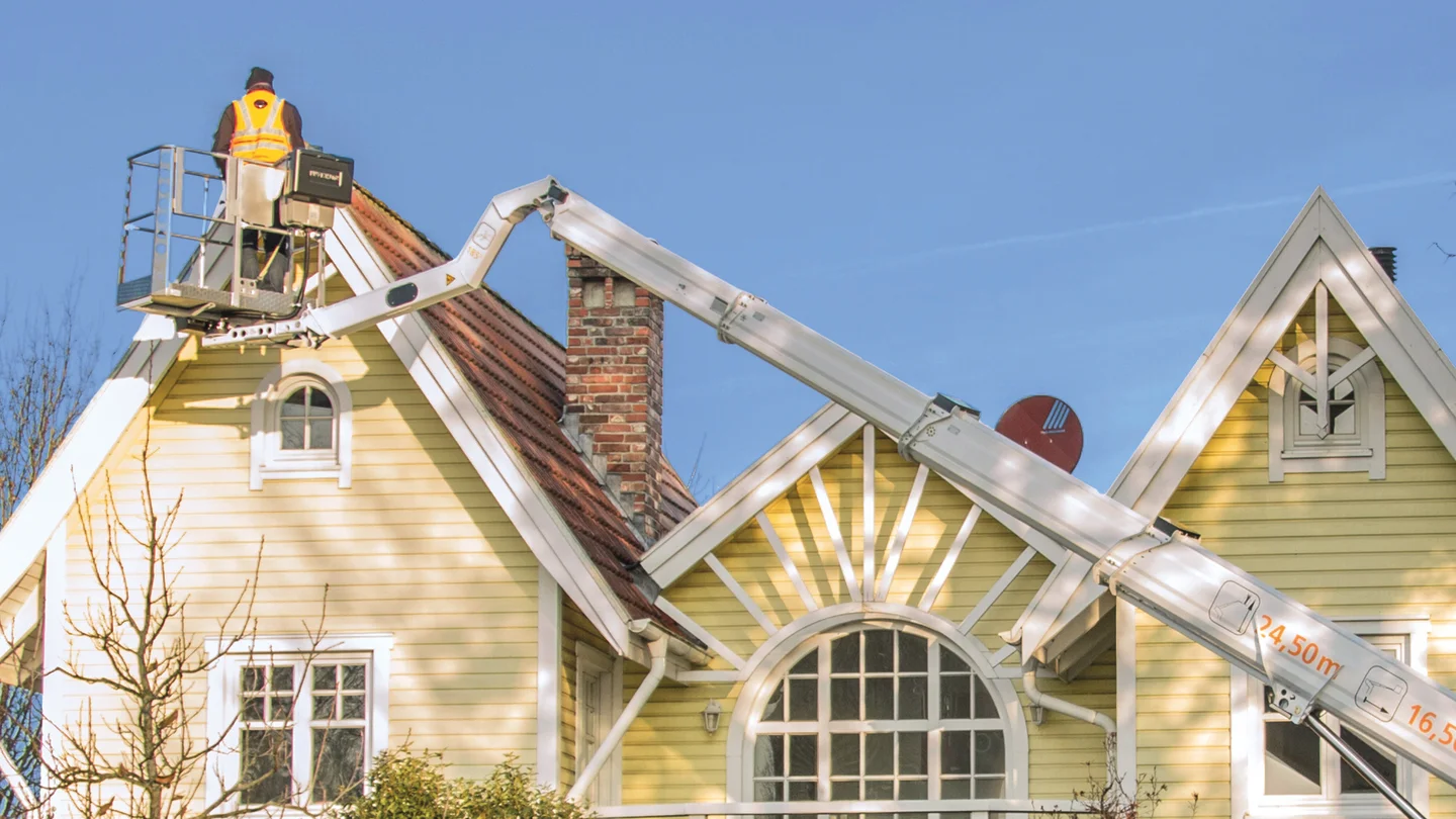 Ausgefahrene Arbeitsbühne vor einem Haus, blauer Himmel im Hintergrund.