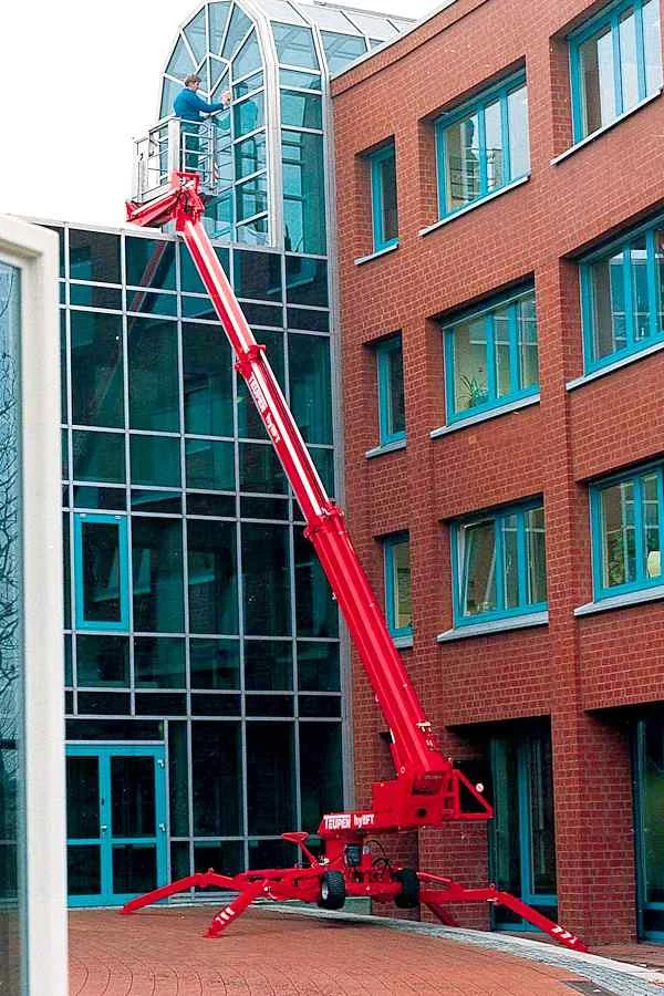 Rote ausgefahrene Arbeitsbühne mit Person vor Fensterfront eines Gebäudes.