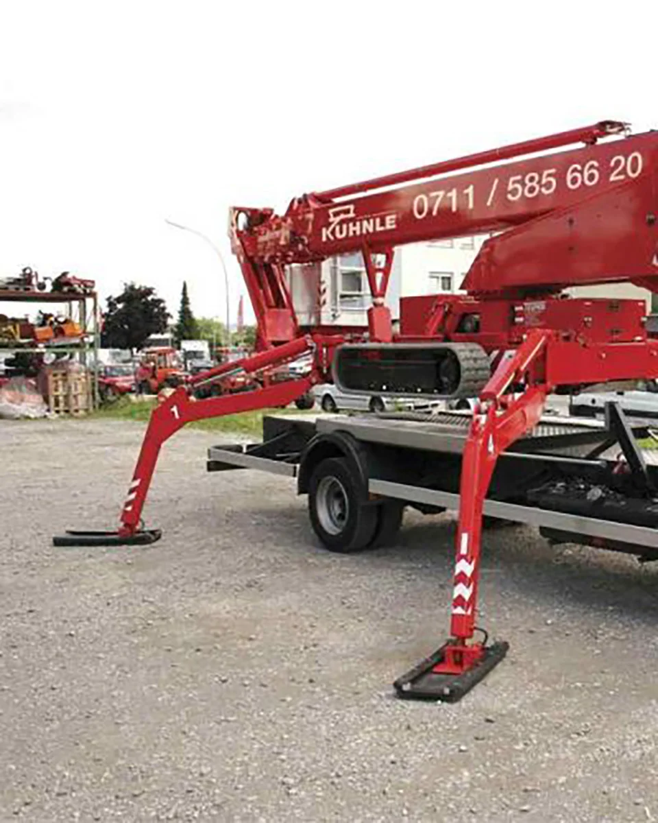 Rote Arbeitsbühne, hinten geparkte Fahrzeuge, Arbeitszubehör und Gebäude