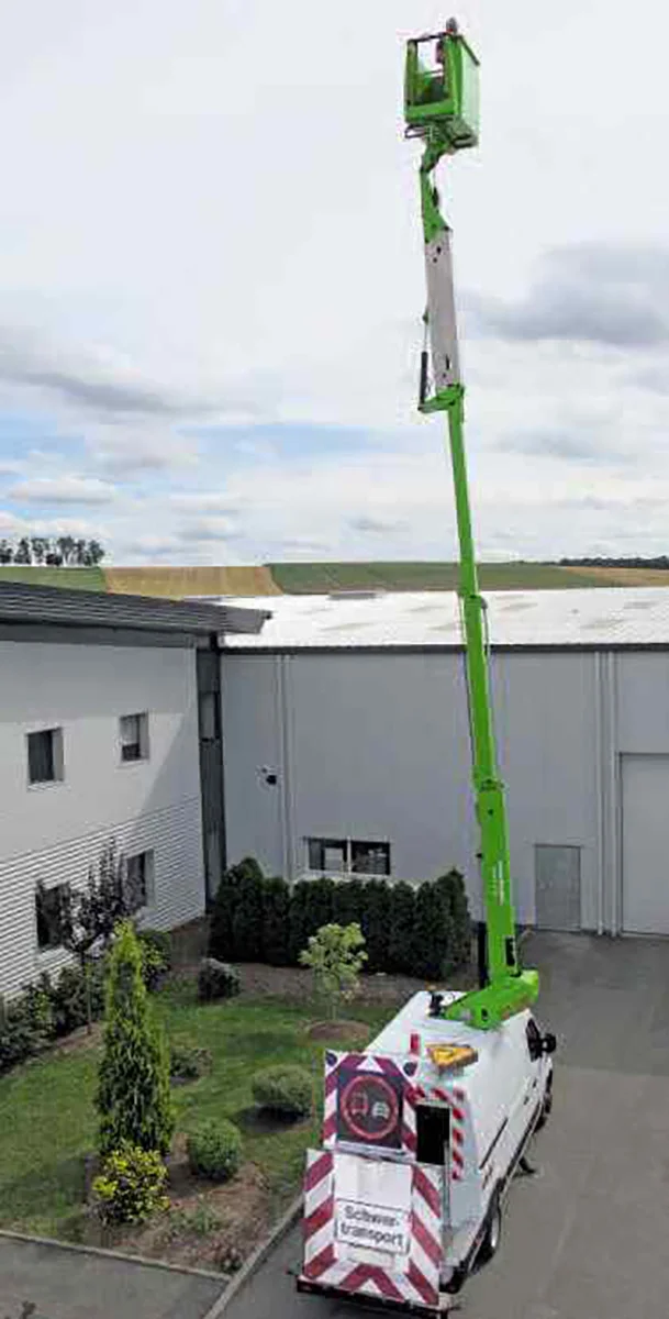 Ausgefahrene Arbeitsbühne im Hof vor weißem Gebäude, draußen bei wolkigem Himmel.