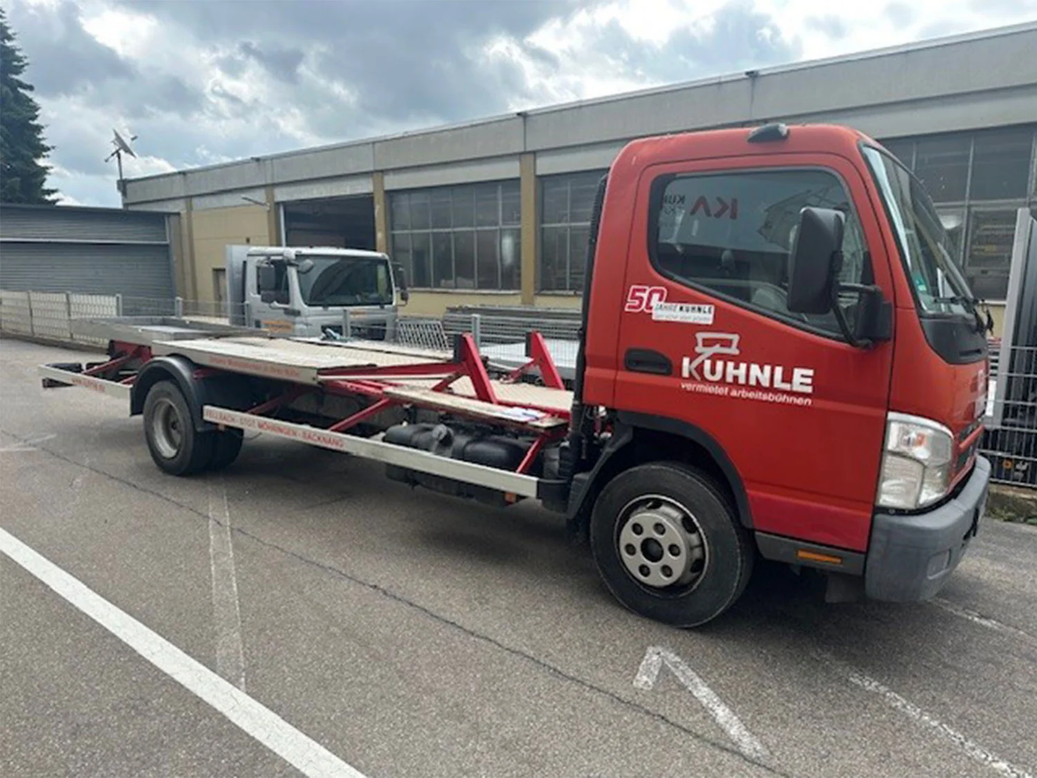 Raupentransporter vor Gebäude, Himmel bewölkt.